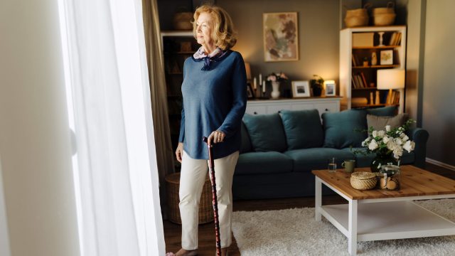 Smiling woman stands near sunny door with help of a cane