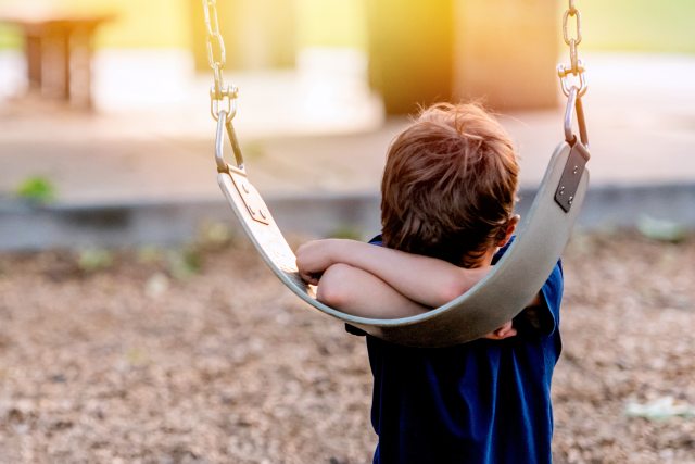 young boy with head in his arms against a playground swing