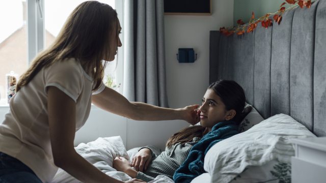 A long-haired adult woman cares for a young person in bed