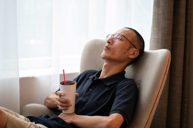 Man with glasses rests in a chair while holding a tumbler in his hand