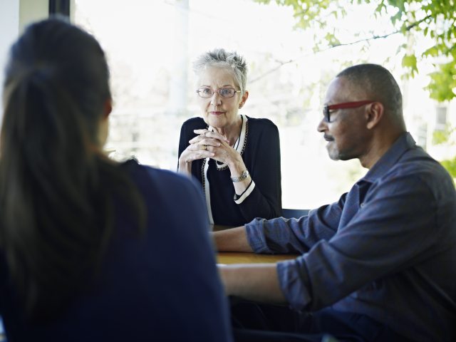 Three people facing each other around a table having a discussion