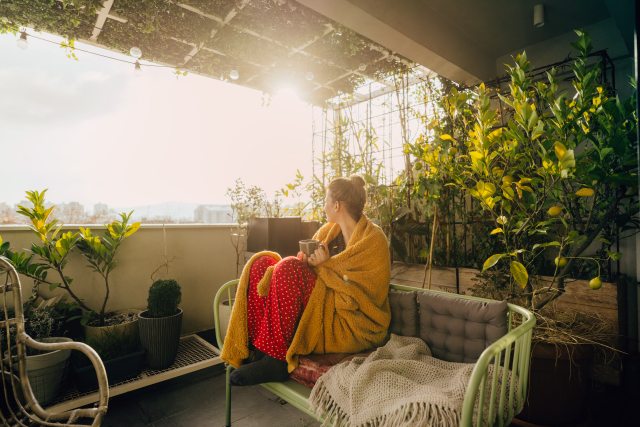Woman sitting on patio with a yellow blanket and cup of tea.