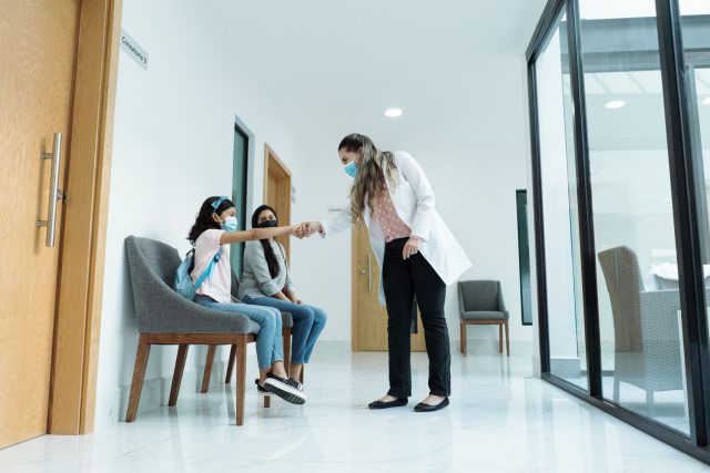 Female doctor greeting young patient and her mom in the hallway of a hospital.