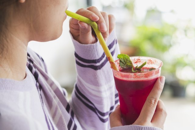Woman drinking a red smoothie out of a glass.
