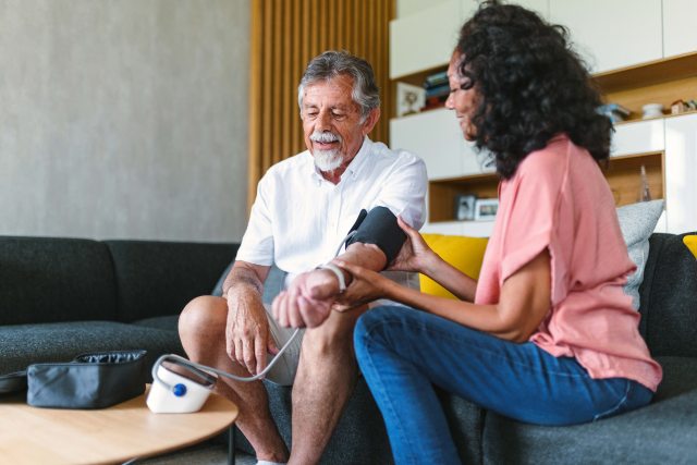 Older man having blood pressure checked by a woman with black hair