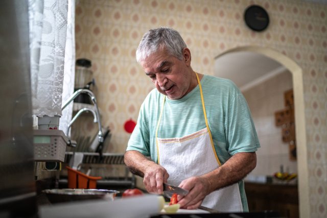 man with short white hair chops veggies in home kitchen