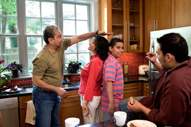 woman and teen boy stand back-to-back to compare heights