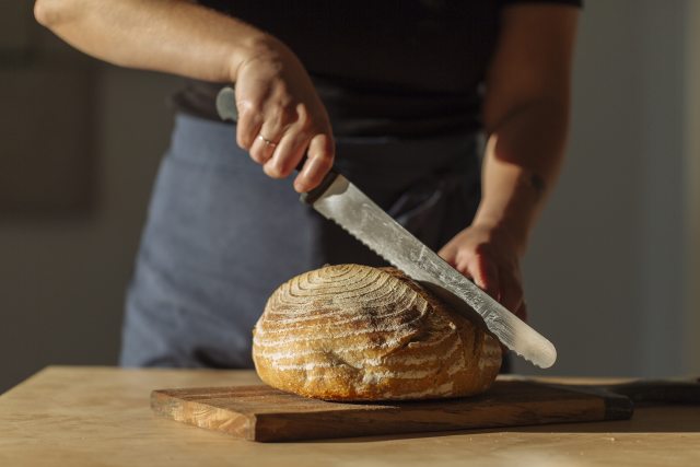 Person cutting a loaf of sourdough bread