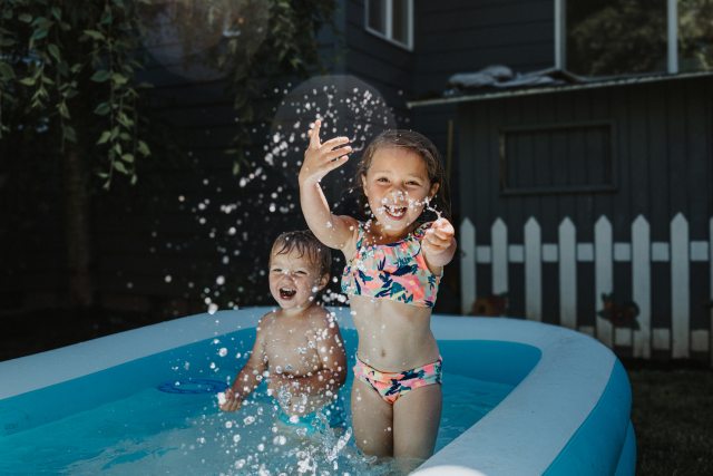 A young boy and girl splash in an inflatable backyard pool.