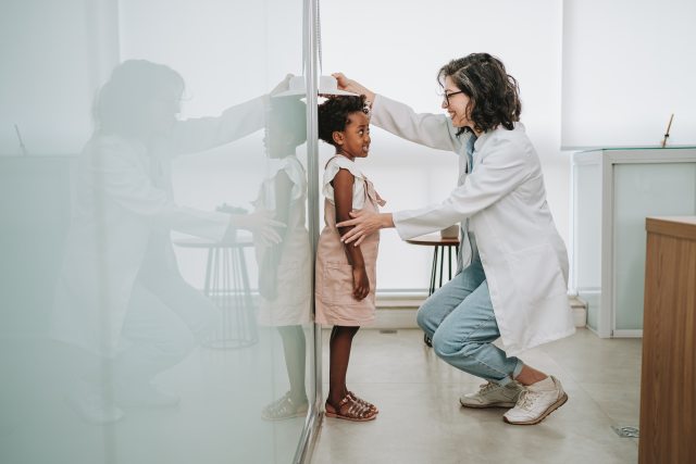 Young girl stands next to wall as doctor measures height