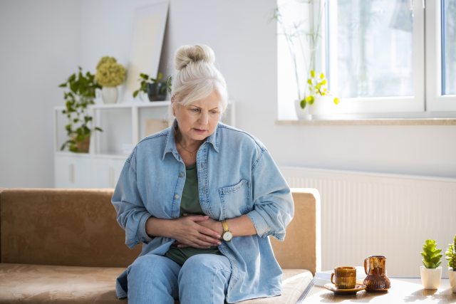 white-haired woman holds hands over stomach as in pain