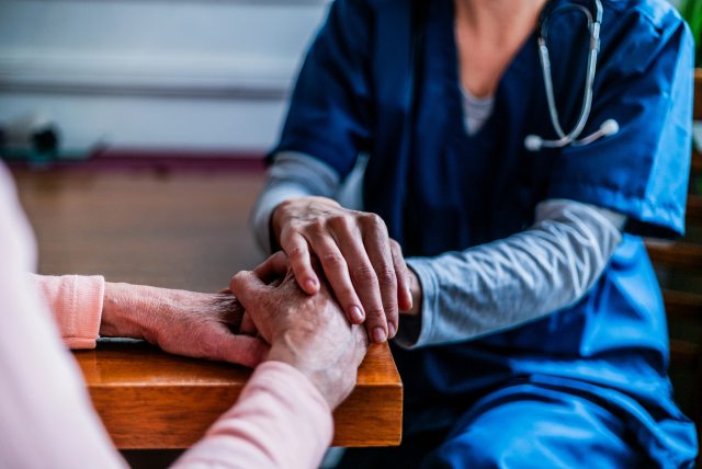 A caregiver holds the hands of an elderly patient