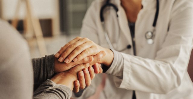 A caregiver holds a patient's hand in a clinical setting as a show of comfort