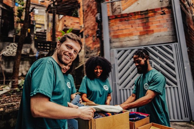 A group of volunteers sort clothing and other donated items in boxes while the person in the foreground smiles at the camera