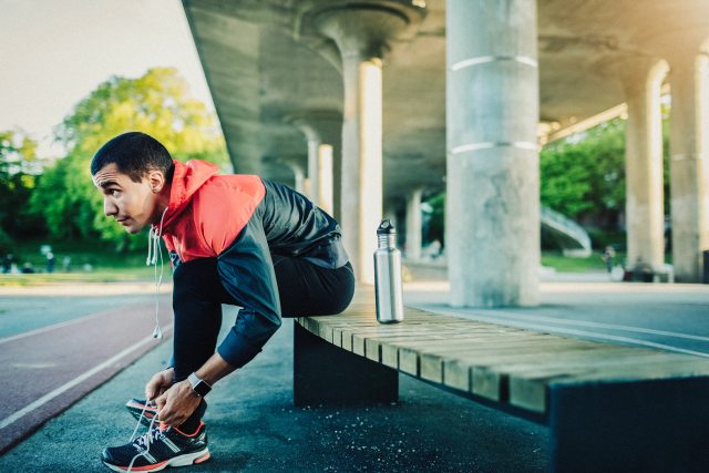 A man sits on a concrete platform and laces up his shoes in preparation for a run