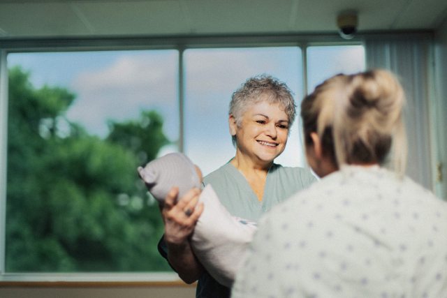 A PeaceHealth caregiver in the background smiles and speaks with a patient in the foreground