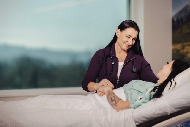 A caregiver sits bedside and comforts patient in a clinical setting