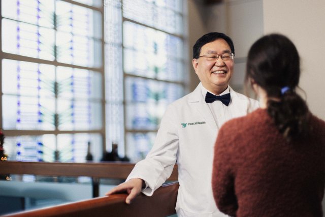 A PeaceHealth provider smiles and listens to a patient in the foreground