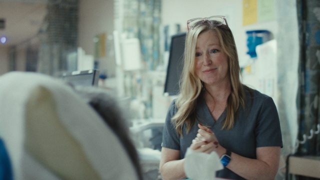 A caregiver smiles and speaks with a patient in a clinical setting
