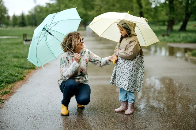 A woman and young girl with umbrellas walking on a sidewalk in the rain