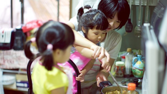 Young girls help adult fix soup in kitchen
