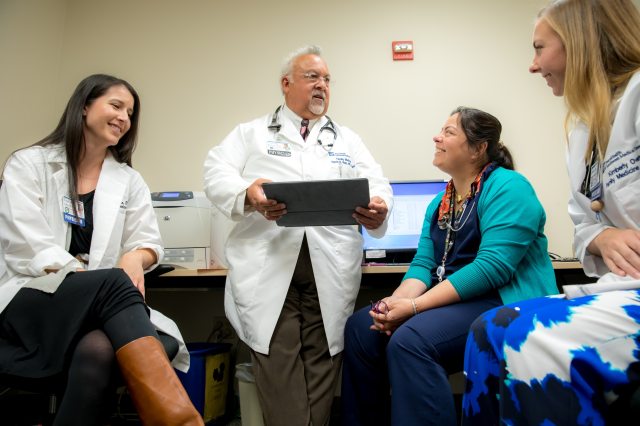 Dr. Ruiz stands and speaks with a group of other providers sitting in a room of computers