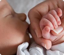 Close-up of adult hand holding a sleeping newborn baby's hand