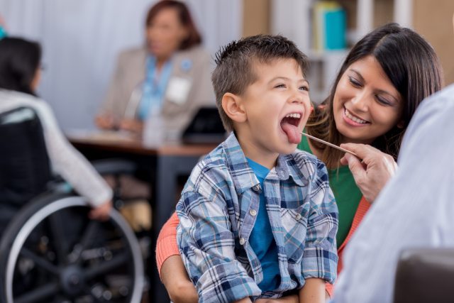 A young boy holds his tongue out as a provider checks his temperature