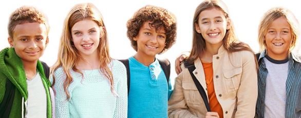 A group of five kids stand shoulder to shoulder smiling