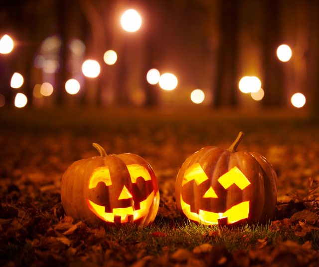 A pair of illuminated jack o' lanterns site on leafy grass at night