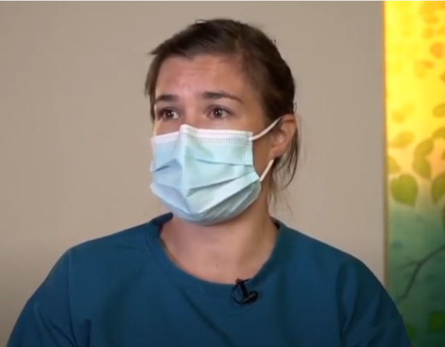 A masked nurse looks on 