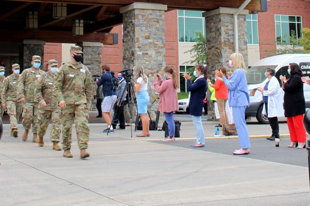 A group of masked PeaceHealth employees claps for masked National Guard members as they march out of the medical center