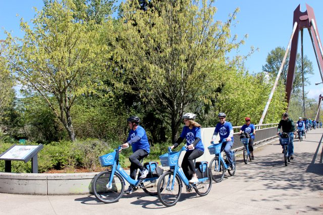 Caregivers cross a bridge on a sunny day on PeaceHealth Rides bicycles