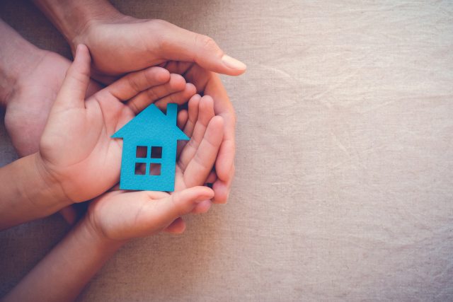 Two pairs of hands hold a cardboard cutout of a blue house