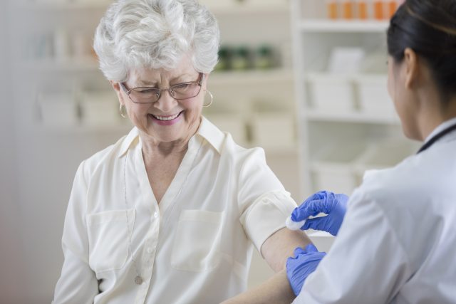 An elderly woman receives a vaccination in her left arm