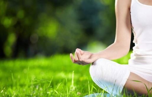 A woman in white performs yoga in a park-like setting.