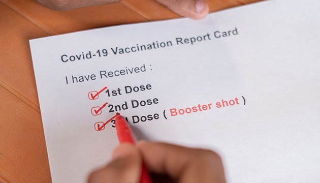 COVID-19 vaccination card in hands showing booster shot box checked