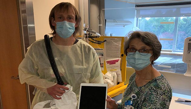 In masks, Chaplain Nettie and Andy Fisher display an Ipad in a patient room.