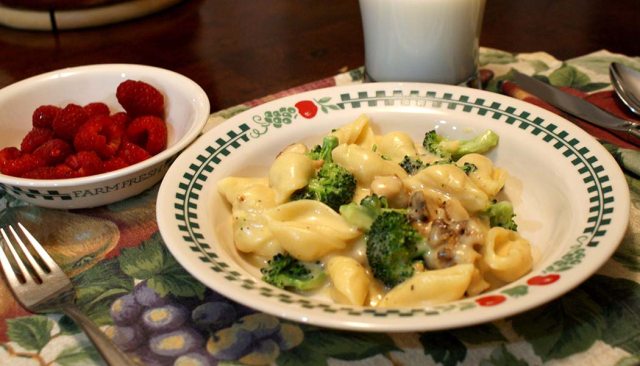A plate of cheesy broccoli with raspberries on the side