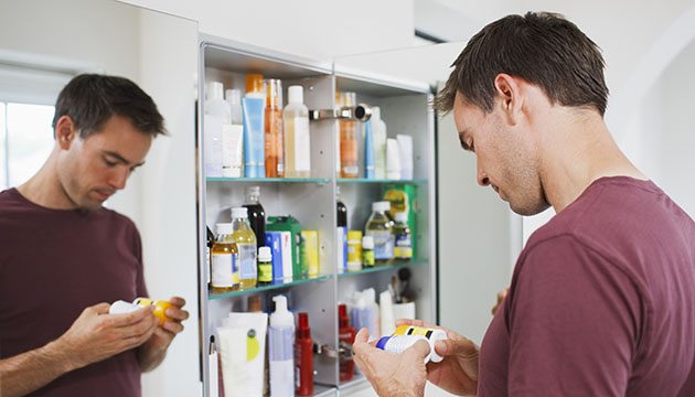 young person examines bottles in front of medicine cabinet