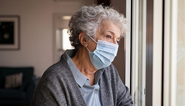 Lonely woman wearing a mask looks out window
