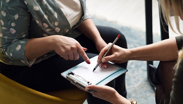 Person points to clipboard held by healthcare provider
