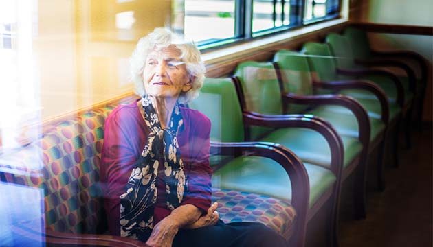 An older lady in purple shirt and scarf looks out a window from her seat