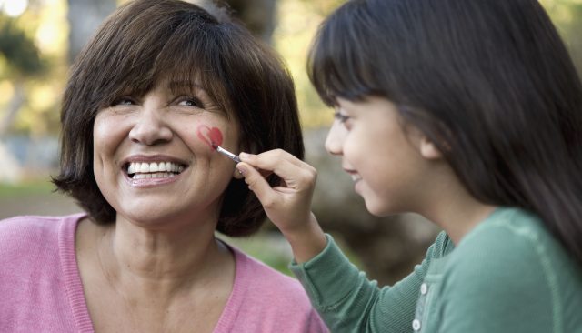 Young person paints heart on cheek of older person