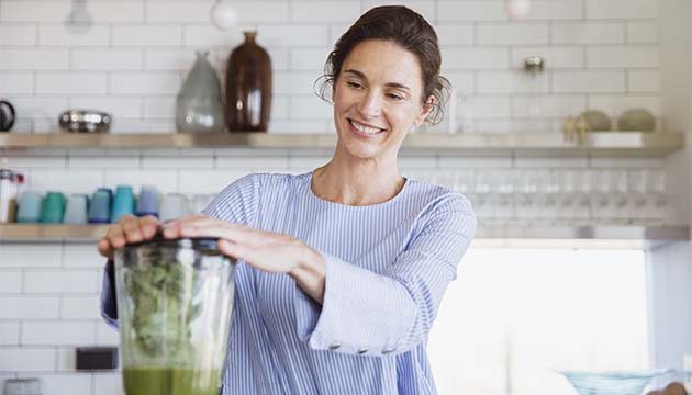 A woman smiles while using a blender