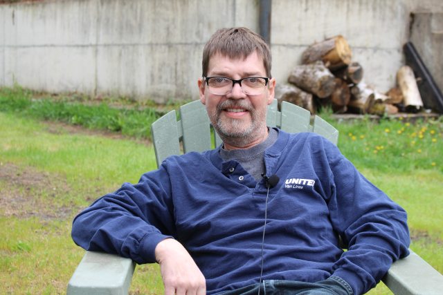 Grant Cunningham sits in a chiar in a fenced yard and smiles