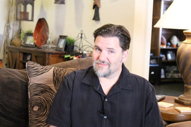 A man in a brown shirt sitting on a living room couch
