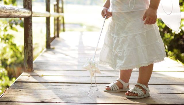 Young child in a white dress holding a toy magic wand with a star on the end