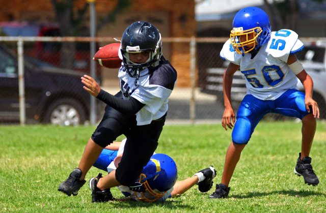 A youth football player runs with a ball around defenders during a game