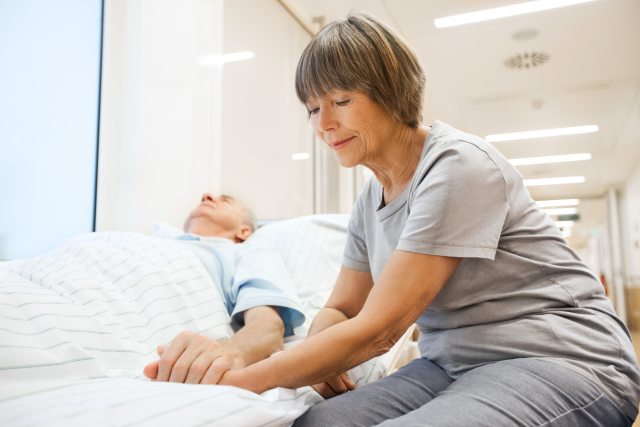 A woman holding the hand of a patient in a hospital bed